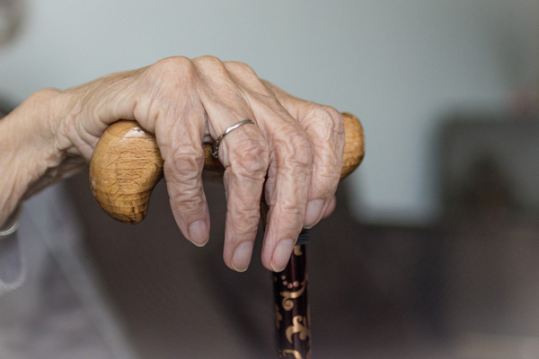 die Hand einer alten Frau, die einen Gehstock aus Holz hält