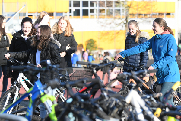 im Vordergrund einige abgestellte Fahrräder, dahinter Schülerinnen vor einem Schulgebäude