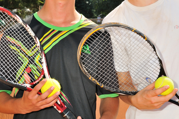 Hände, die zwei Tennisschläger und zwei Tennisbälle halten