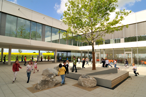 einen Schulhof mit spielenden Kindern, im Hintergrund Schulgebäude