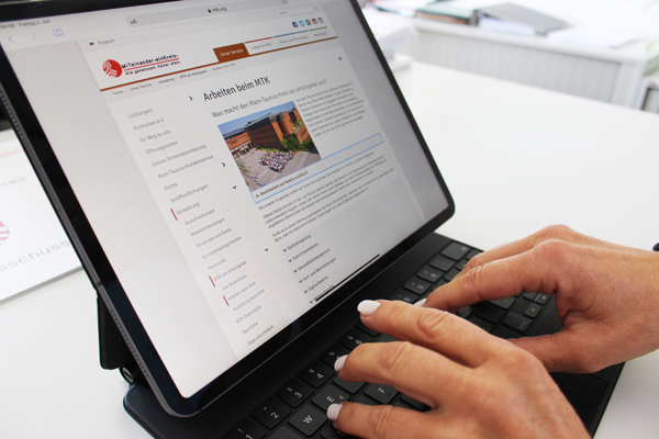 ein Tablet, auf dem die Webseite mtk.org mit dem Inhalt Arbeiten beim MTK geöffnet ist, und Hände, die darauf tippen