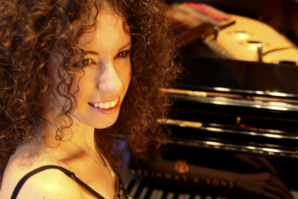 Portrait einer Frau mit dunklen Locken, die im Abendkleid an einem Klavier sitzt