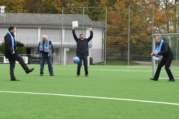 vier Männer mit einem Fußball auf einem Kunstrasenplatz