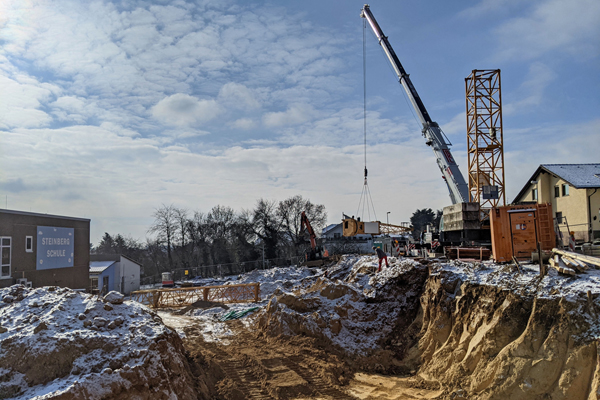 eine Baustelle mit einem Kran neben einer Grube mit ersten Erdarbeiten, es liegt ein wenig Schnee