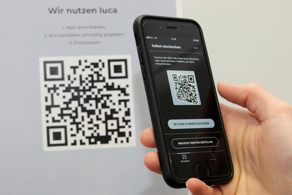 ein Plakat der Smartphone-App luca mit einem QR-Code, der mit einem Smartphone gescannt wird