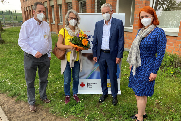 zwei Männer und zwei Frauen, eine mit Blumenstrauß in der Hand, auf einer Wiese vor einem Backstein-Gebäude