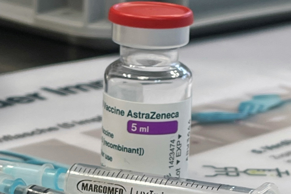 ein Fläschchen mit Impfstoff von AstraZeneca, vor dem eine Spritze liegt