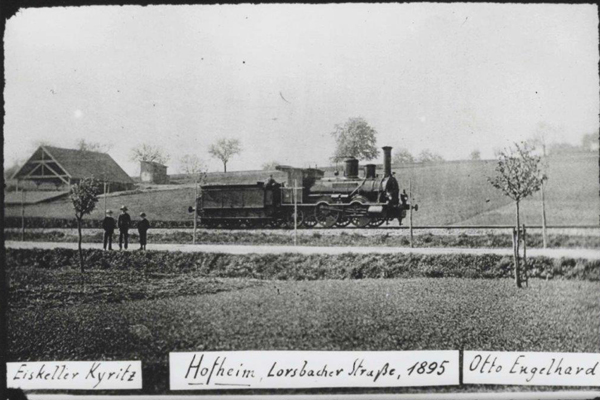 eine alte Schwarzweiß-Fotografie einer fahrenden Lokomotive mit dem Text Eiskeller Kyritz, Lorsbacher Straße in Hofheim aus dem Jahr 1895