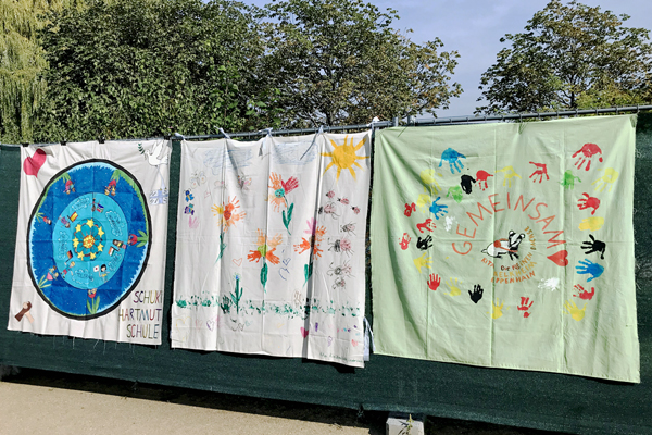 drei bunt bemalte Stoff-Banner an einem Bauzaun