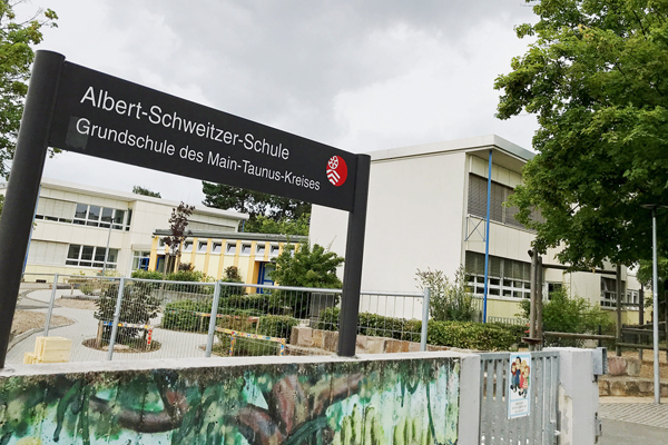 den Blick in einen Innenhof mit Wegen und Büschen und im Vordergrund ein Schild mit dem Text Albert-Schweitzer-Schule