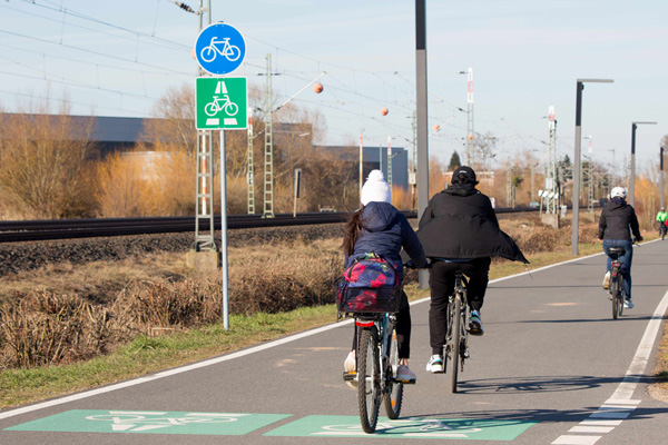 mehrere Fahrradfahrer auf einem beschilderten Radweg neben einem Bahngleis