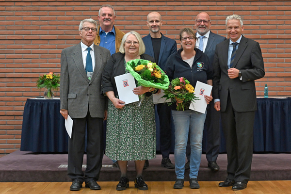 ein Gruppenbild mit fünf Männern und zwei Frauen; einige Personen hatlen Urkunden in den Händen, die beiden Frauen bunte Blumensträuße