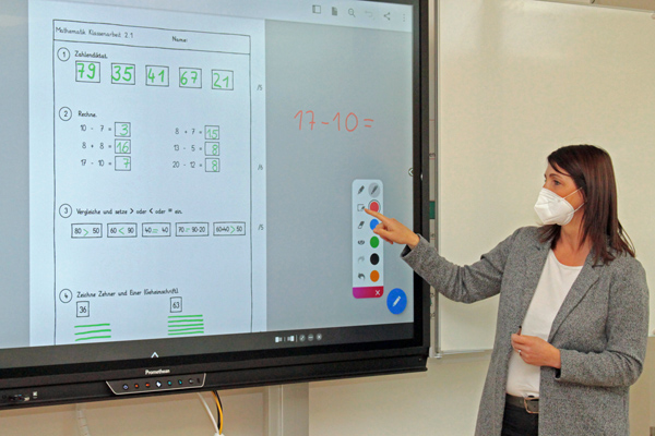 eine dunkelhaarige Frau, die an einer digitalen Tafel eine Mathematik-Klassenarbeit demonstriert
