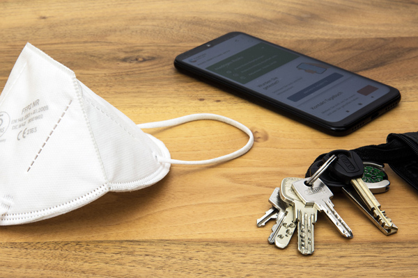 eine FFP2-Maske auf einem Tisch neben einem Schlüsselbund und einem Smartphone mit geöffneter Corona-Warn-App