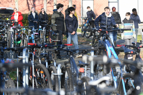 im Vordergrund eine große Zahl geparkter Fahrräder und im Hintergrund einige Schüler, von denen manche ein Fahrrad schieben