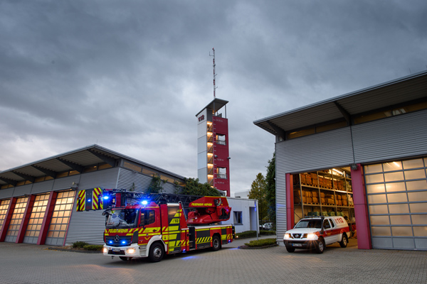 eine Feuerwache mit zwei Feuerwehrautos vor einem dunkel bewölkten Himmel