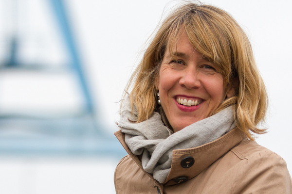 eine blonde Frau in beigem Mantel und mit Schal