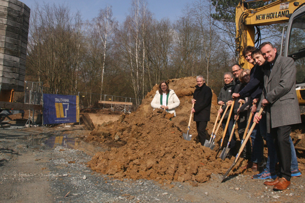 acht Personen auf einer Baustelle, die Spaten in einen Erdhaufen stecken
