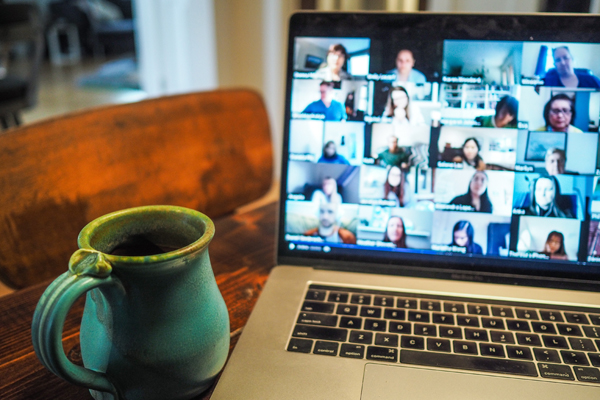 eine Tasse und einen Laptop, auf dem Teilnehmer eines Online Meetings gezeigt werden