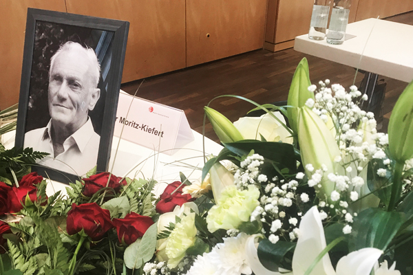 einen Tisch voller Blumen und einen Bilderrahmen mit einem schwarz weiß Portrait eines alten Mannes mit Namensschild