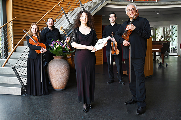 eine Gruppe von fünf Musikern mit Instrumenten und Notenblatt in einem Saal