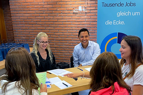 fünf Personen sitzen um einen Tisch mit Unterlagen, in der Ecke steht ein Banner mit der Aufschrift