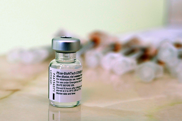 eine Impfdosis Biontech, im Hintergrund ein Haufen Spritzen