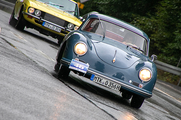 zwei Oldtimer Autos im Regen auf einer nassen Straße