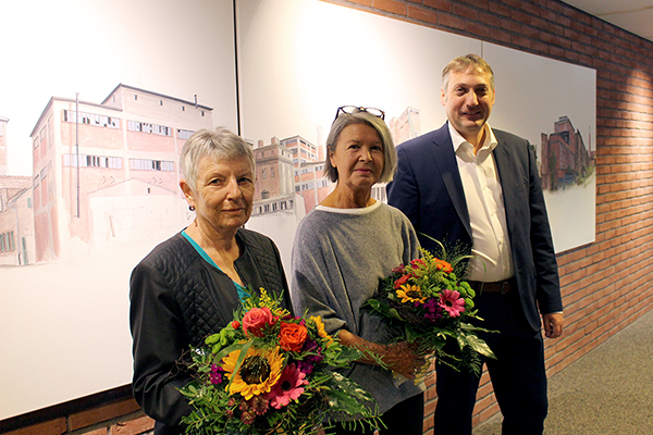 ein Mann und zwei Frauen, die Frauen haben Blumensträuße in der Hand, im Hintergrund sind Gemälde an der Wand