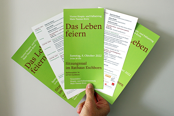 eine Hand hält grün weiße Flyer mit der Aufschrift