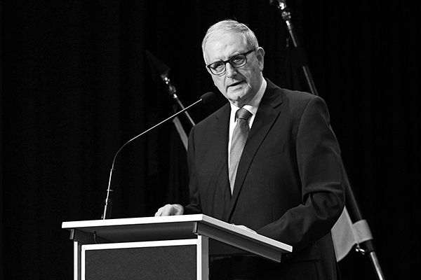 ein älterer Mann spricht an einem Podium, das Motiv ist schwarzweiss