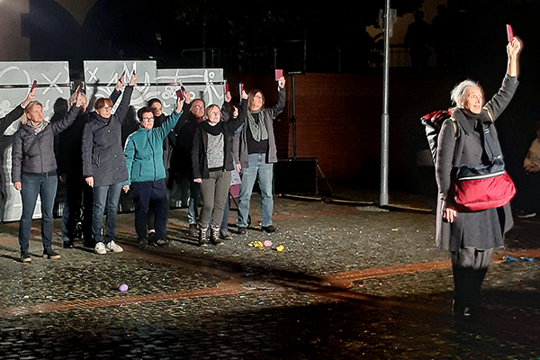 eine große Gruppe Menschen stehen vor einer Mauer und halten eine rote Karte nach oben