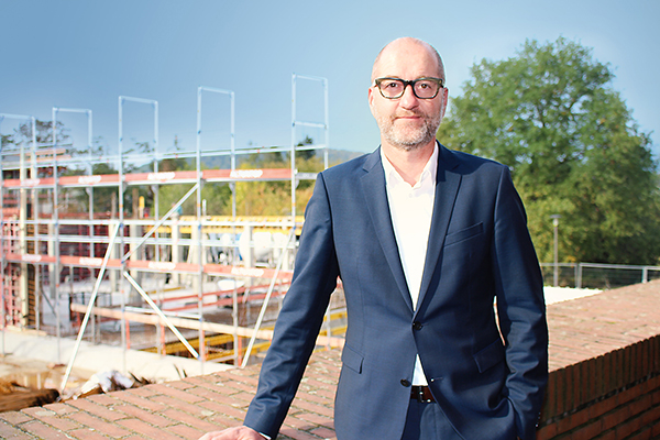 ein Mann mit blauem Anzug und Brille steht vor Baugerüsten