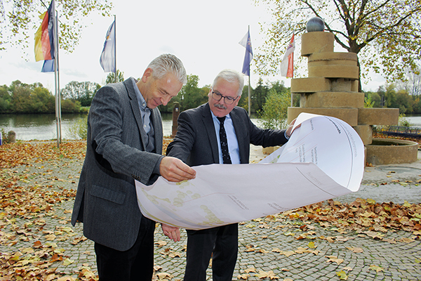 zwei Männer stehen vor einem Ufer mit Flaggen und halten einen Plan aus Papier