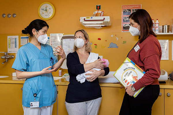 drei Frauen mit Maske, eine Frau hält ein Baby