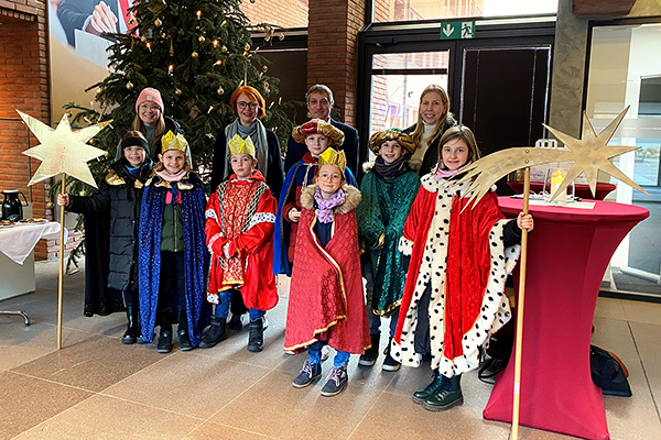 Sieben als Sternsinger verkleidete Kinder und vier Erwachsene stehen vor einem Weihnachtsbaum