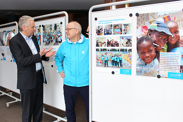 zwei ältere Herren unterhalten sich vor ein paar Aufstellern mit Unicef Plakaten