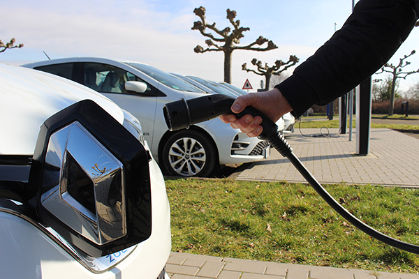 eine Hand steckt ein Ladekabel in ein E-Auto