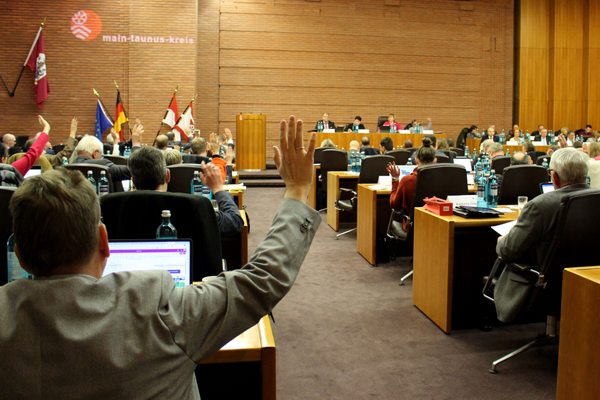 viele Menschen in einem großen Saal, mehrere heben die Hand