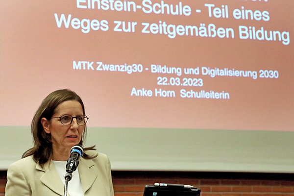 eine Frau an einem Rednerpult, dahinter ist eine Präsentation zu