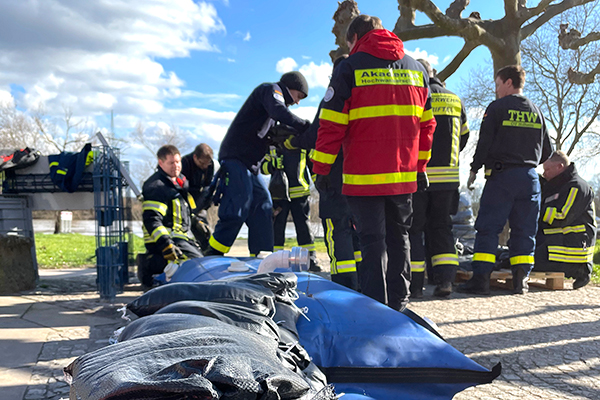eine Reihe Sandsäcke mit einer Gruppe Feuerwehrmännern im Hintergrund bei der Übung