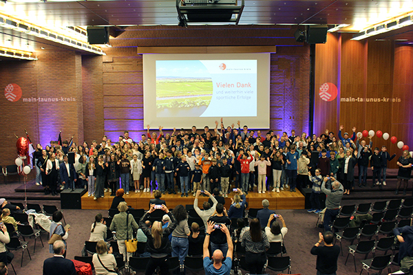 ein voller Saal mit einer großen Menge an Menschen auf einer Bühne für ein Gruppenbild