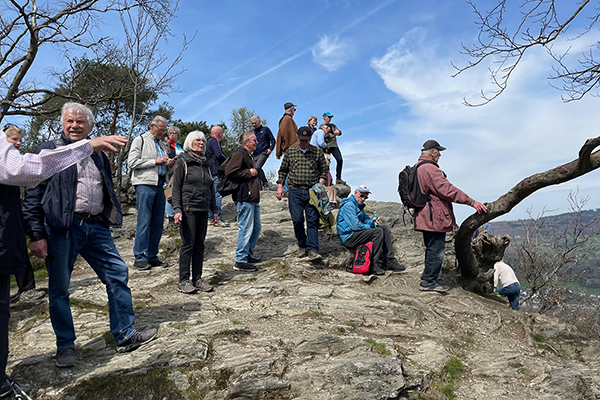 eine große Gruppe Wanderer auf einem Berggipfel bei Sonnenschein