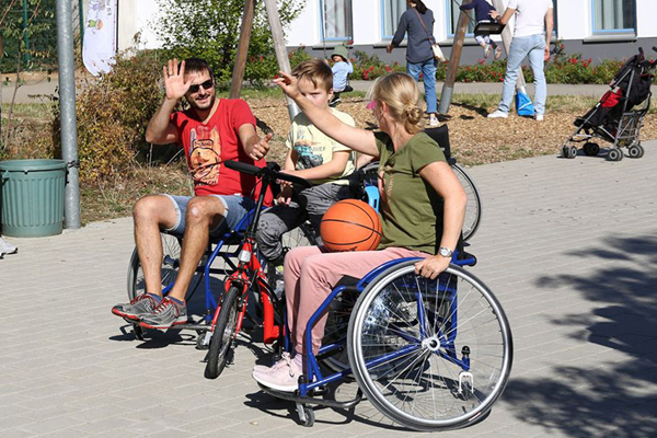 zwei Erwachsene und ein Kind, die Erwachsenen sitzen im Rollstuhl und das Kind auf dem Fahrrad