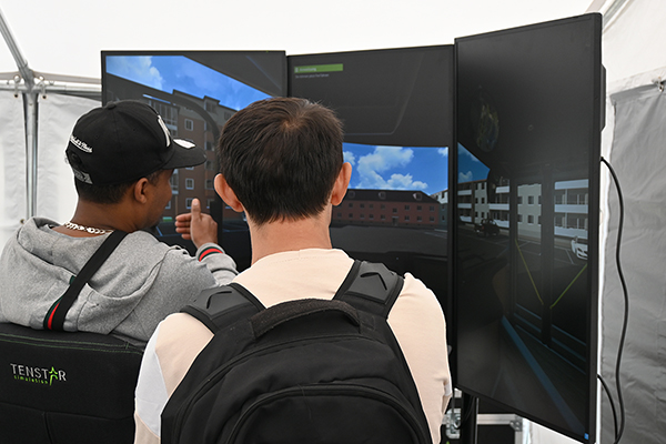 zwei junge Männer sind von hinten zu sehen und sitzen vor einem Fahrsimulator