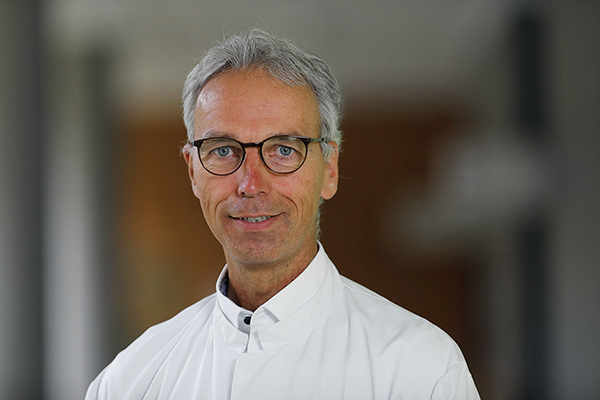 Portrait von einem Mann mit weißen Haaren, weißem Hemd und einer Brille