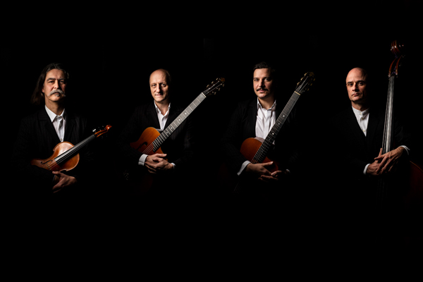 vier Musiker in einer Reihe vor schwarzem Hintergrund, jeder von ihnen hält ein Instrument