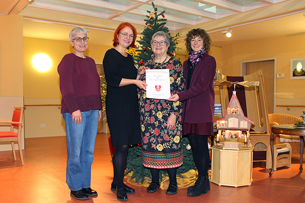 vier Frauen vor einem Weihnachtsbaum halten eine Urkunde in der Hand