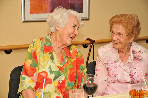 zwei lachende Bewohnerinnen eines Seniorenheims im Gespräch.