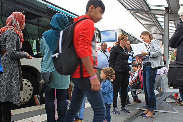Flüchtlingsfamilien, die in Busse einsteigen und dabei von einer Frau eingewiesen werden.